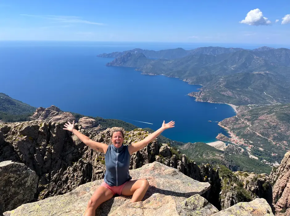 Christina jubelt auf Felsen über einer Meeresbucht